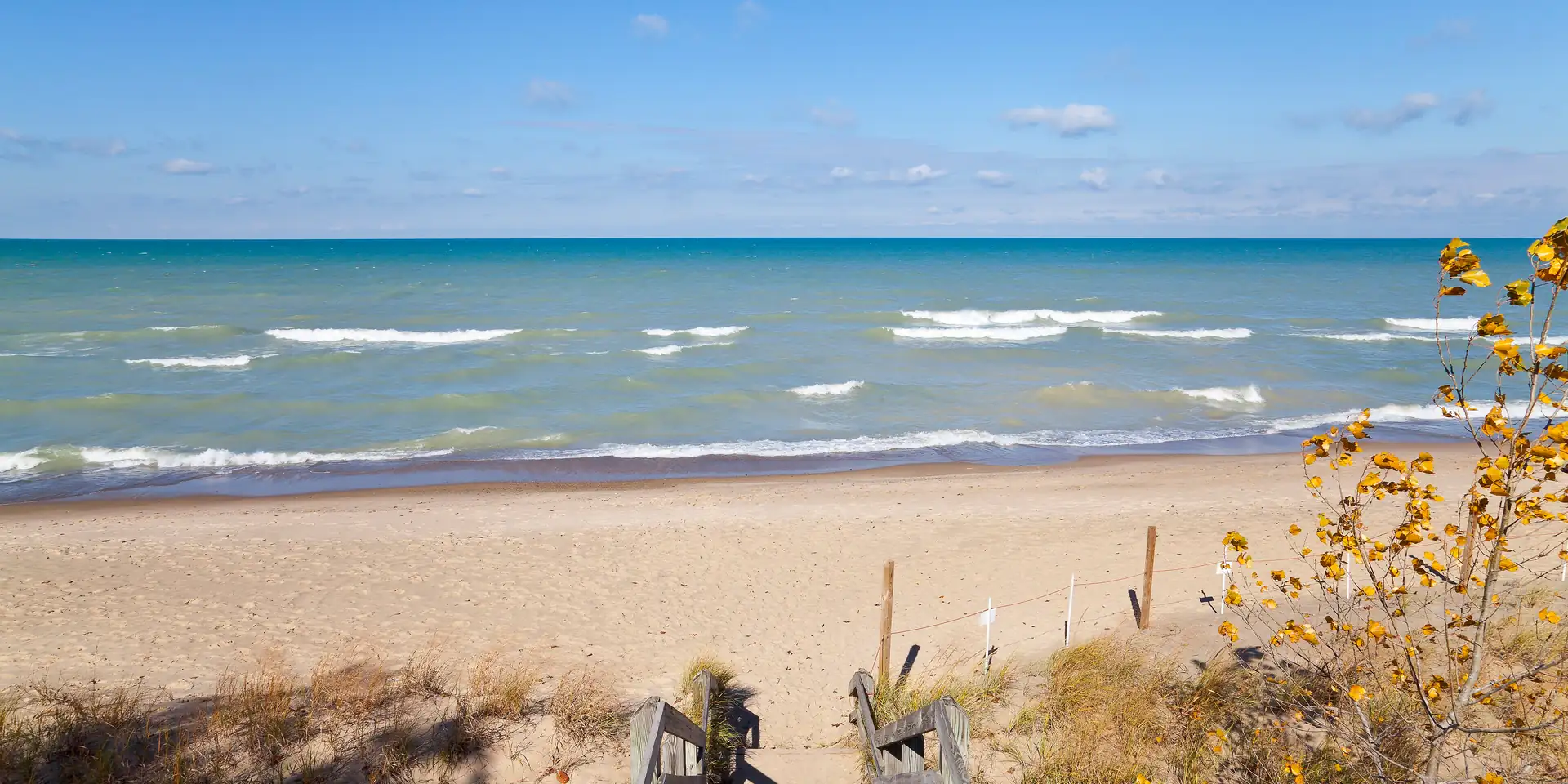 Lake Michigan surf rolling onto a sand beach at Indiana Dunes, reached by a wooden stair through the dune grass